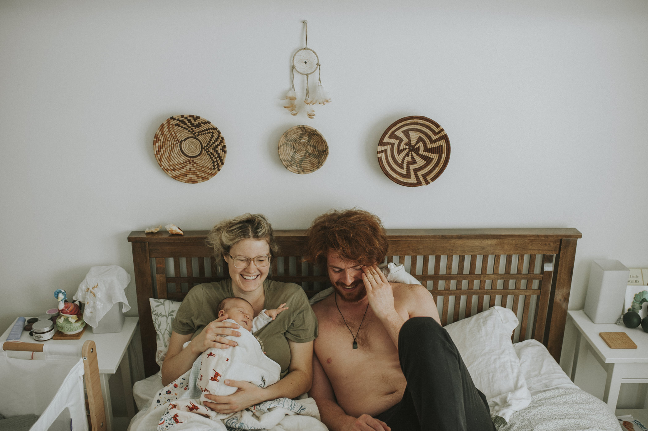 couple with newborn baby, in bed. Couple laughing. 